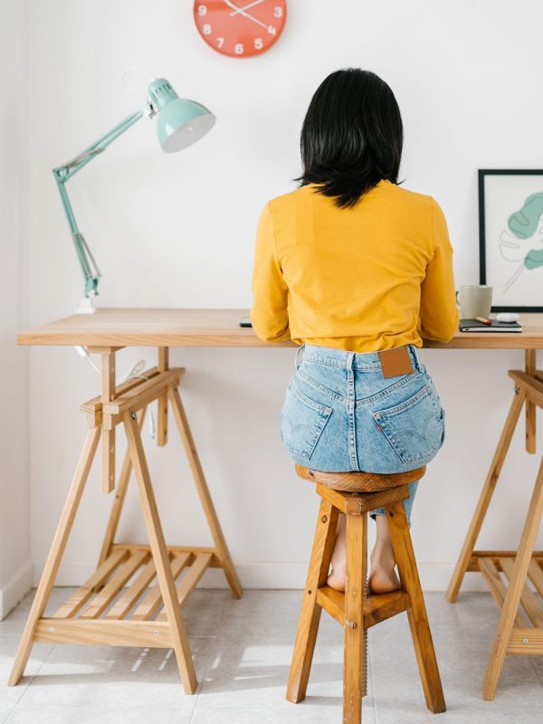 Back view of young woman sitting on a workplace while working from home. Business and home office concept.