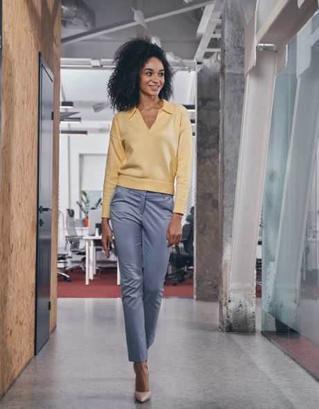 Full-sized portrait of a slender woman with a gadget in her hand walking along the corridor