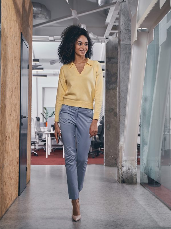 Full-sized portrait of a slender woman with a gadget in her hand walking along the corridor