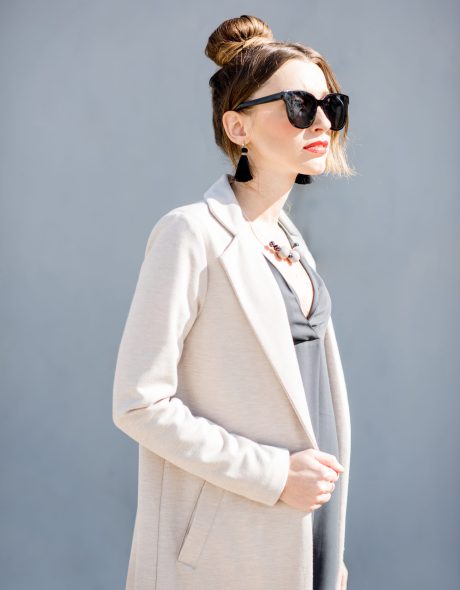 Lifestyle portrait of an elegant business woman dressed in coat on the blue wall background outdoors