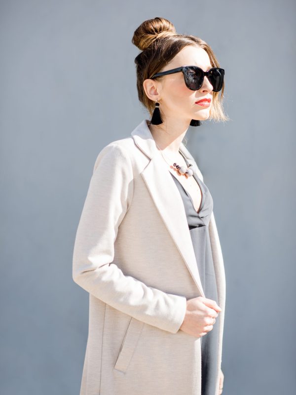 Lifestyle portrait of an elegant business woman dressed in coat on the blue wall background outdoors